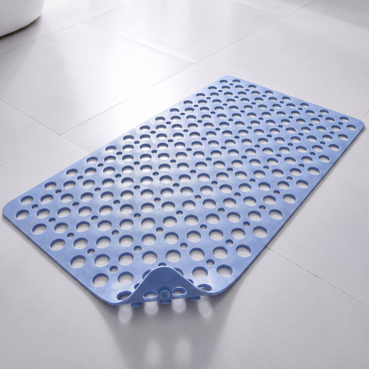 Tapis de douche antidérapant bleu clair à trous et ventouses, posé à plat sur un sol carrelé