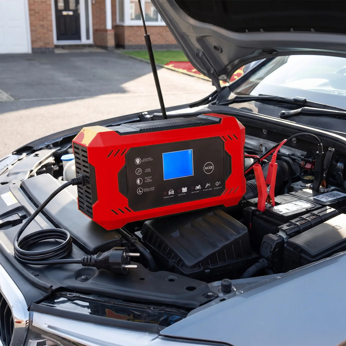 Chargeur de batterie coloris rouge posé sur la batterie sous le capot