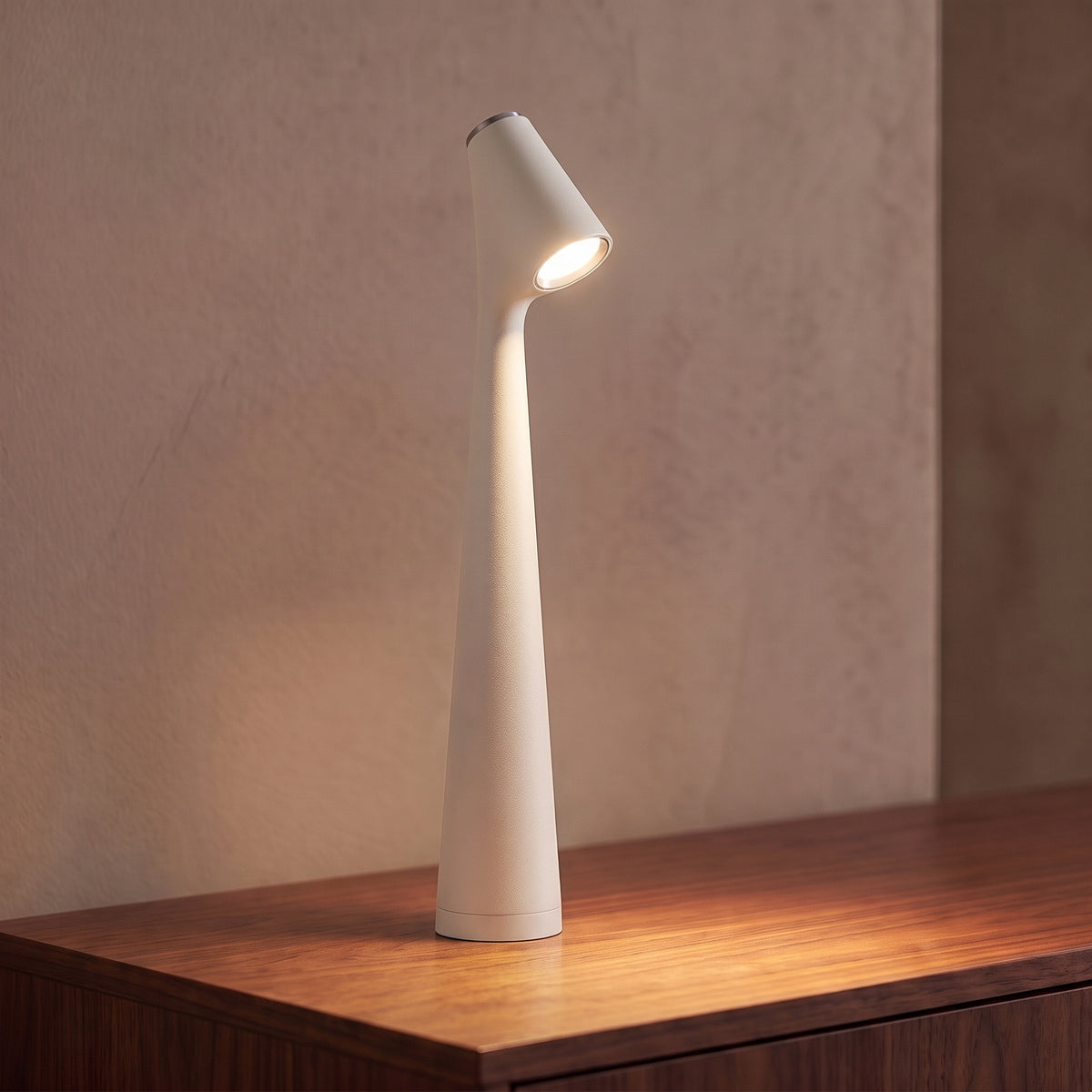 Lampe sans fil rechargeable blanche en aluminium mat allumée sur une console en noyer, tête inclinée tournée vers l'objectif