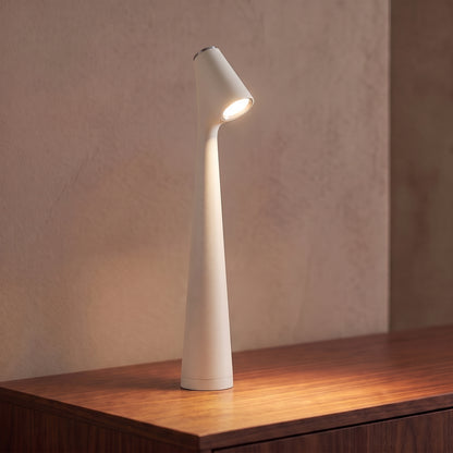 Lampe sans fil rechargeable blanche en aluminium mat allumée sur une console en noyer, tête inclinée tournée vers l'objectif