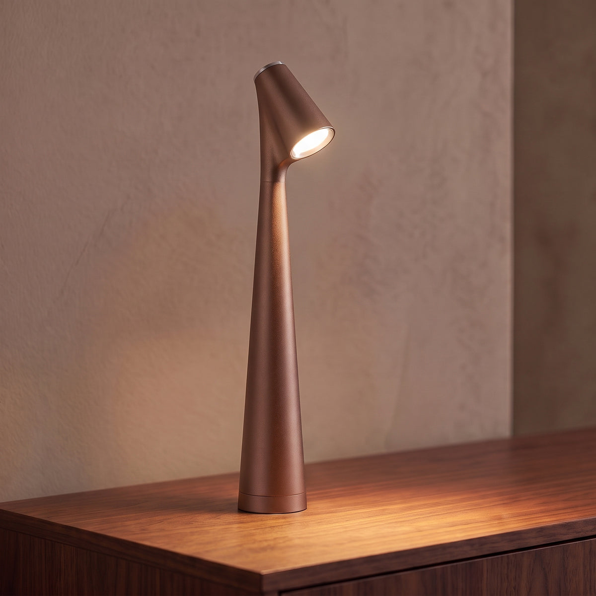 Lampe sans fil rechargeable marron bronze en aluminium mat allumée sur une console en noyer, tête inclinée tournée vers l'objectif