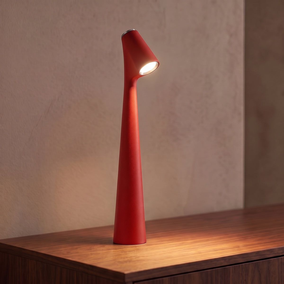 Lampe sans fil rechargeable rouge en aluminium mat allumée sur une console en noyer, tête inclinée tournée vers l'objectif