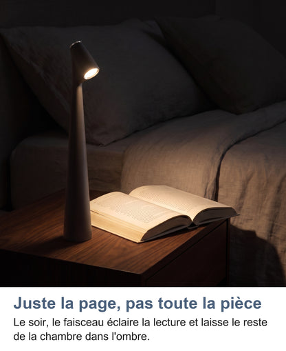 Lampe noire allumée sur une table de nuit, faisceau sur un livre ouvert