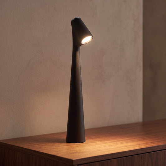 Lampe sans fil rechargeable noire en aluminium mat allumée sur une console en noyer, tête inclinée tournée vers l'objectif