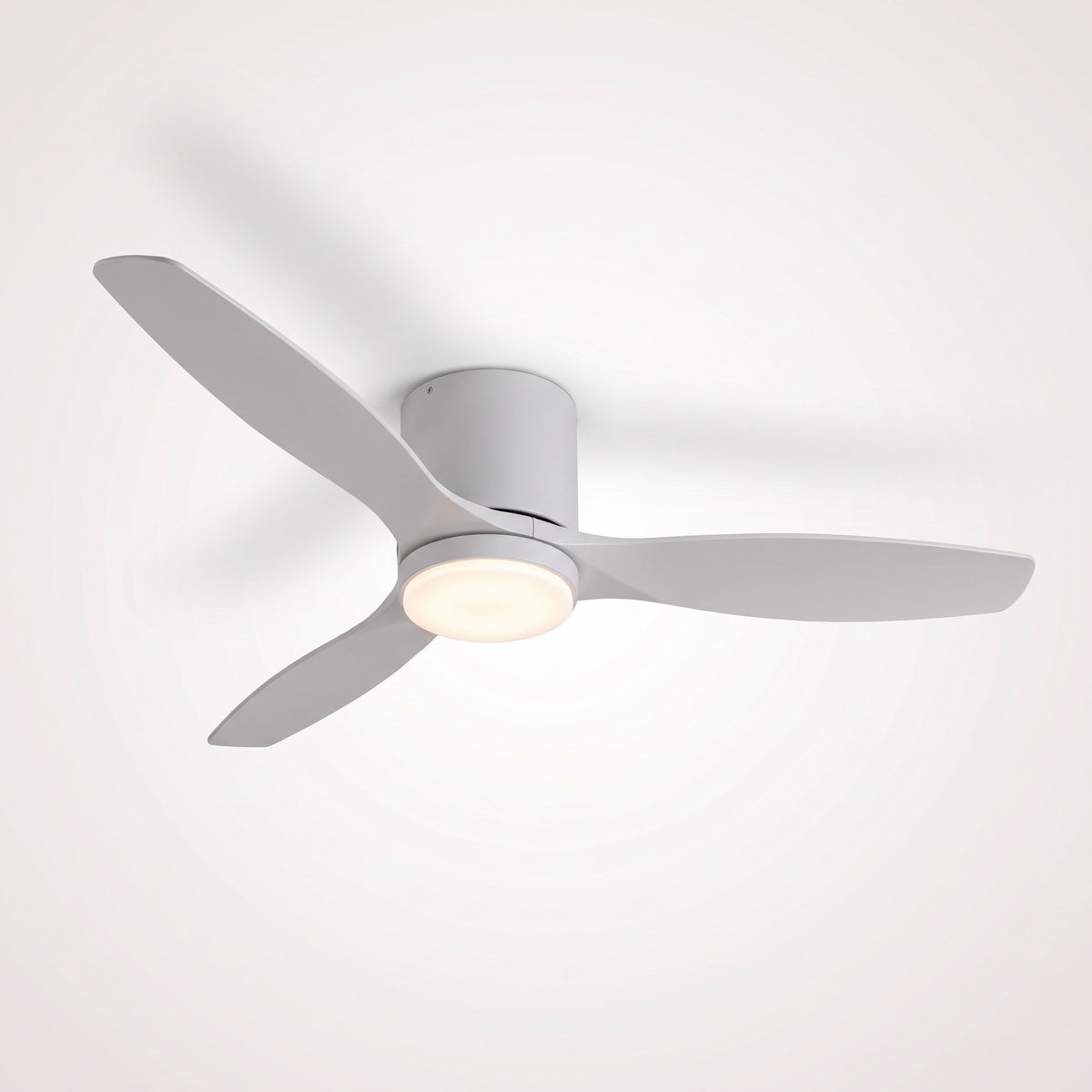 Ventilateur de plafond blanc à trois pales blanches et disque LED allumé, vu de trois quarts sous un plafond clair