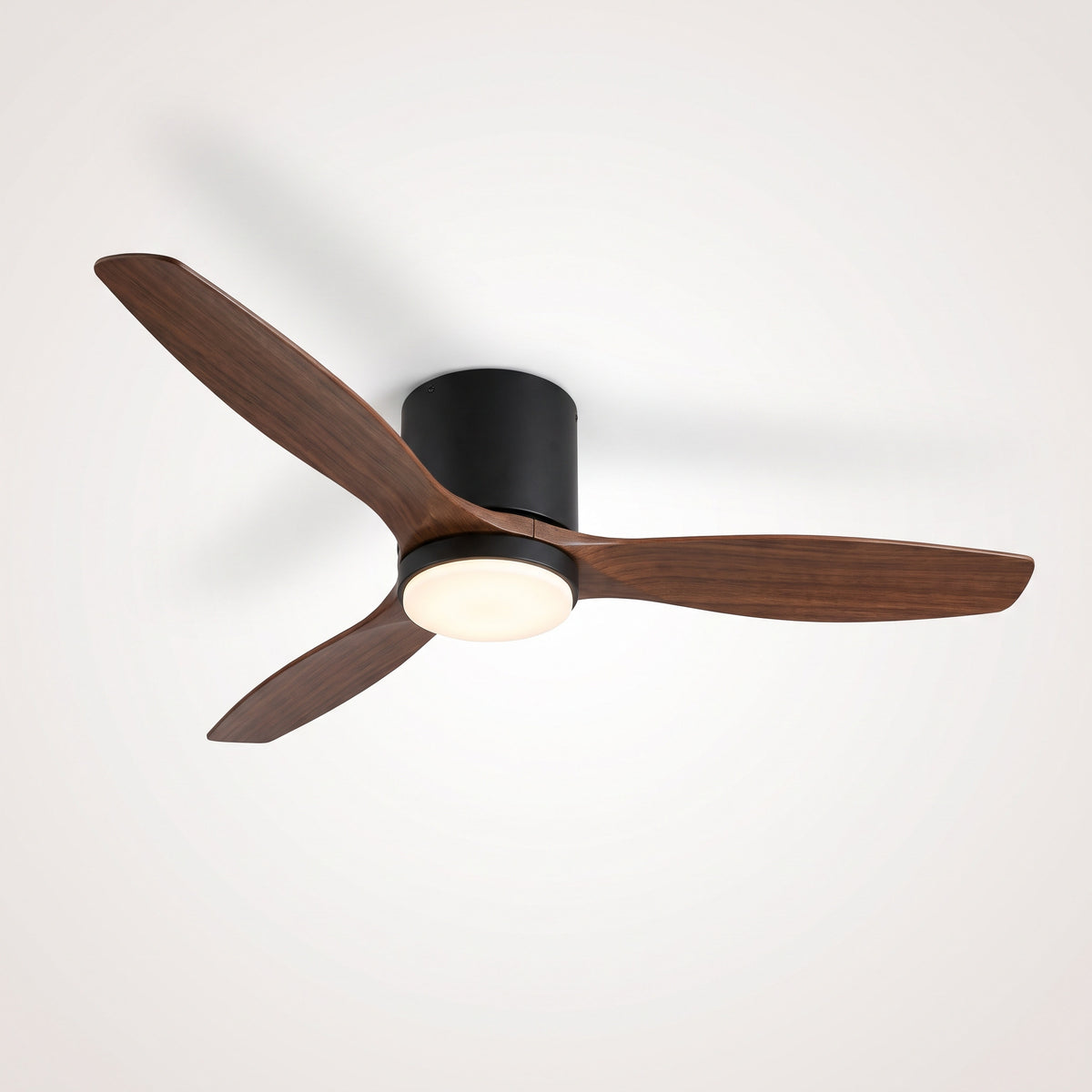Ventilateur de plafond noir à trois pales en bois foncé et disque LED allumé, vu de trois quarts sous un plafond clair