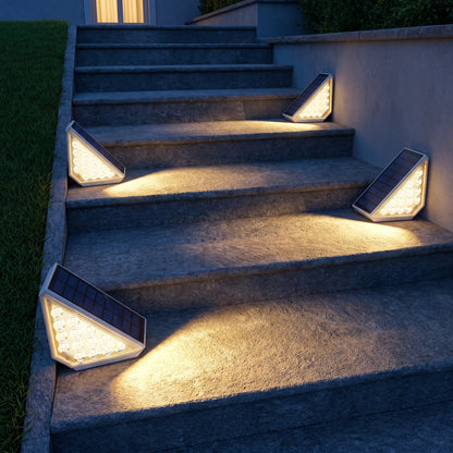 Quatre spots solaires allumés sur un escalier extérieur en pierre la nuit, lumière blanc chaud sur chaque marche
