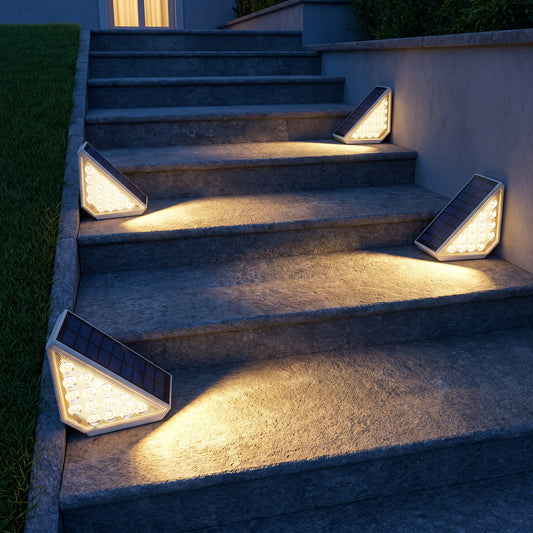 Quatre spots solaires allumés sur un escalier extérieur en pierre la nuit, lumière blanc chaud sur chaque marche